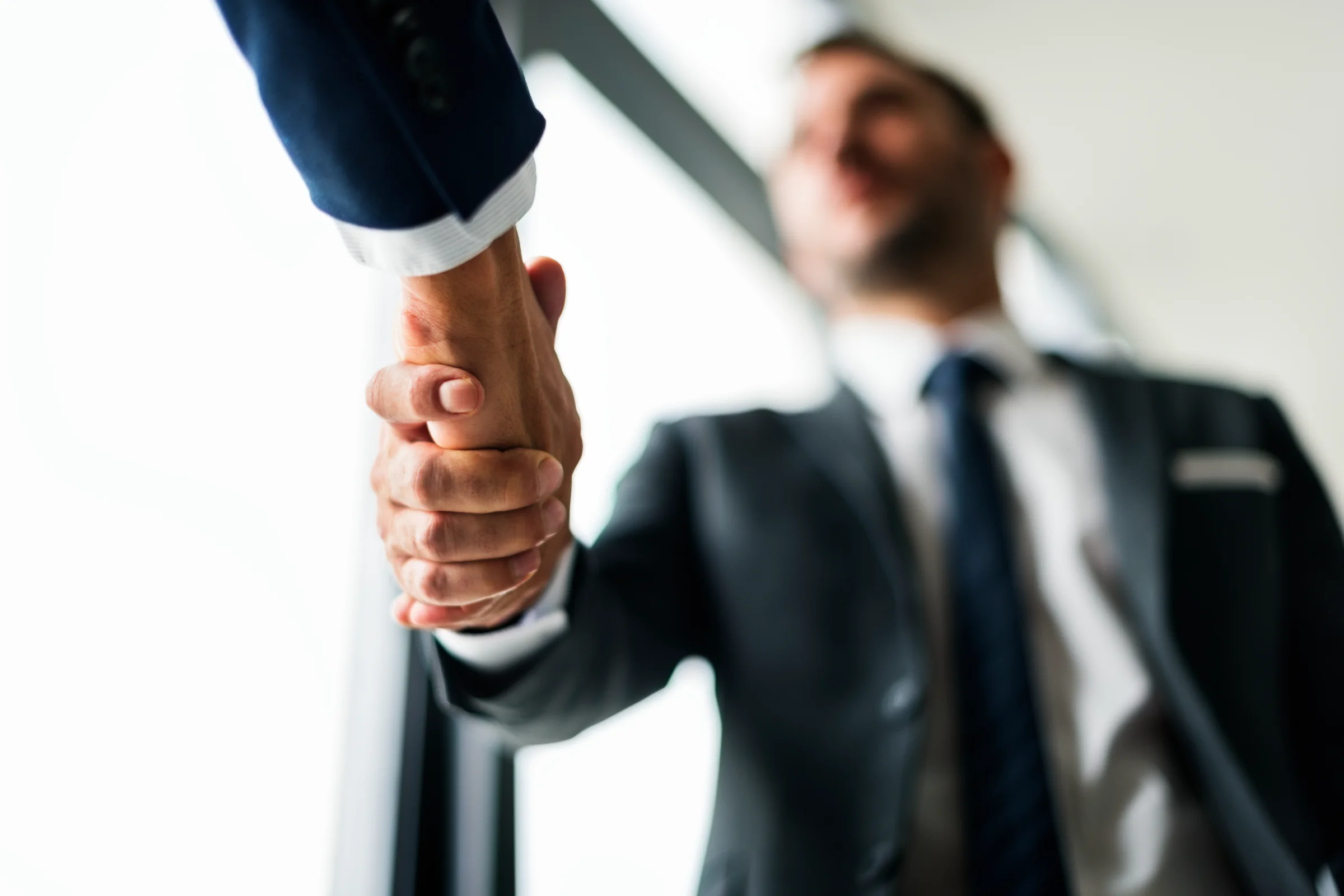Two people in suits shaking hands near a window, symbolizing a business agreement or partnership.
